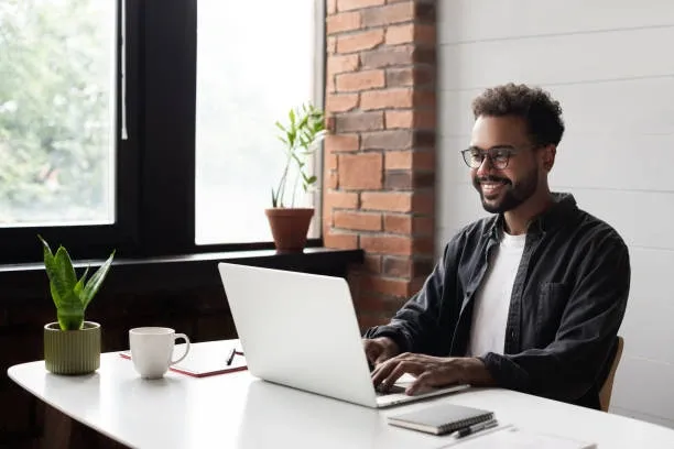 Man working on a laptop in a cozy office with brick walls.