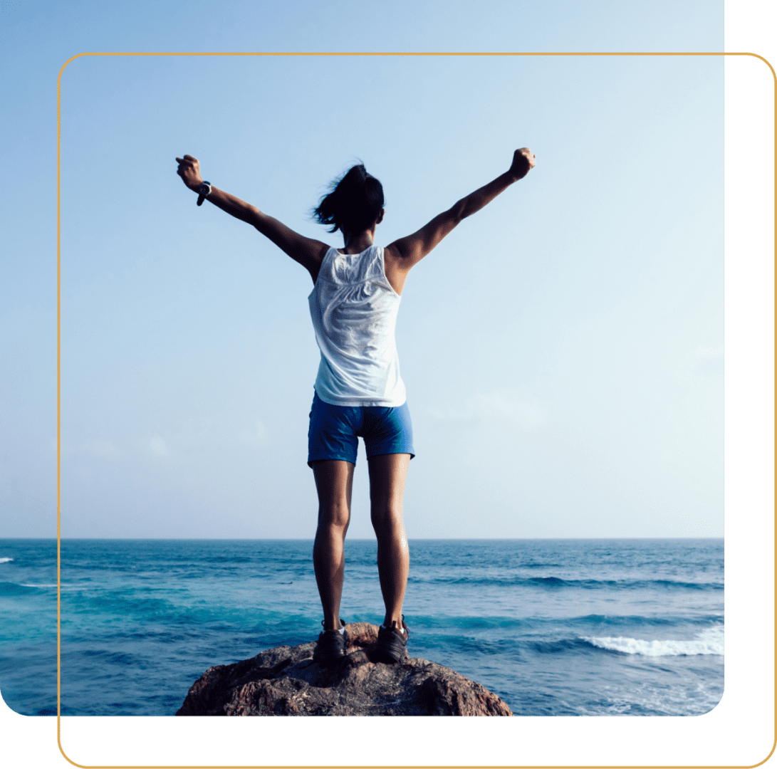 Person standing on a rock with arms raised by the ocean under a clear sky. Person standing on a rock with arms raised by the ocean under a clear sky.