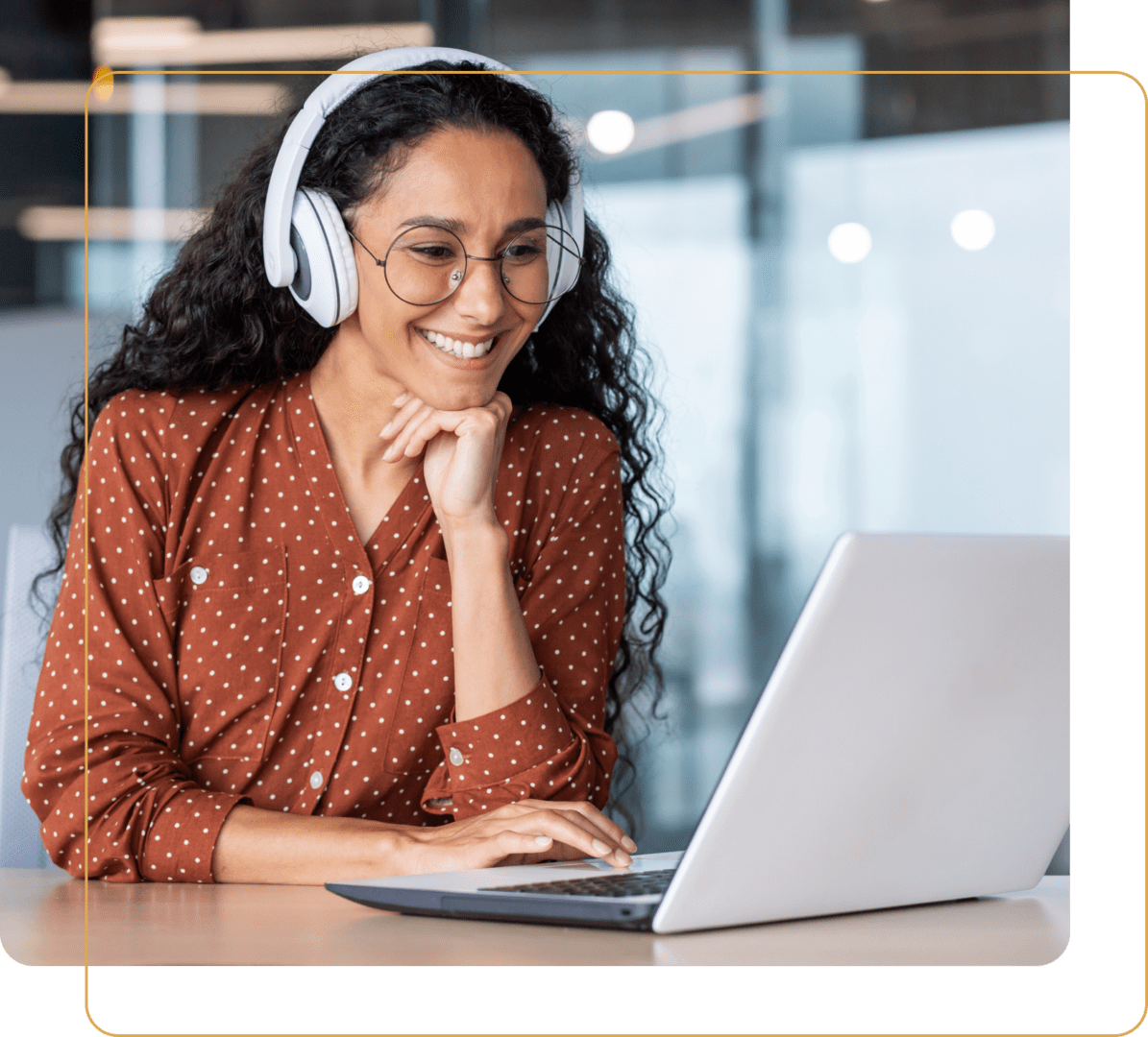 A woman wearing headphones and glasses smiles at a laptop screen indoors. A woman wearing headphones and glasses smiles at a laptop screen indoors.