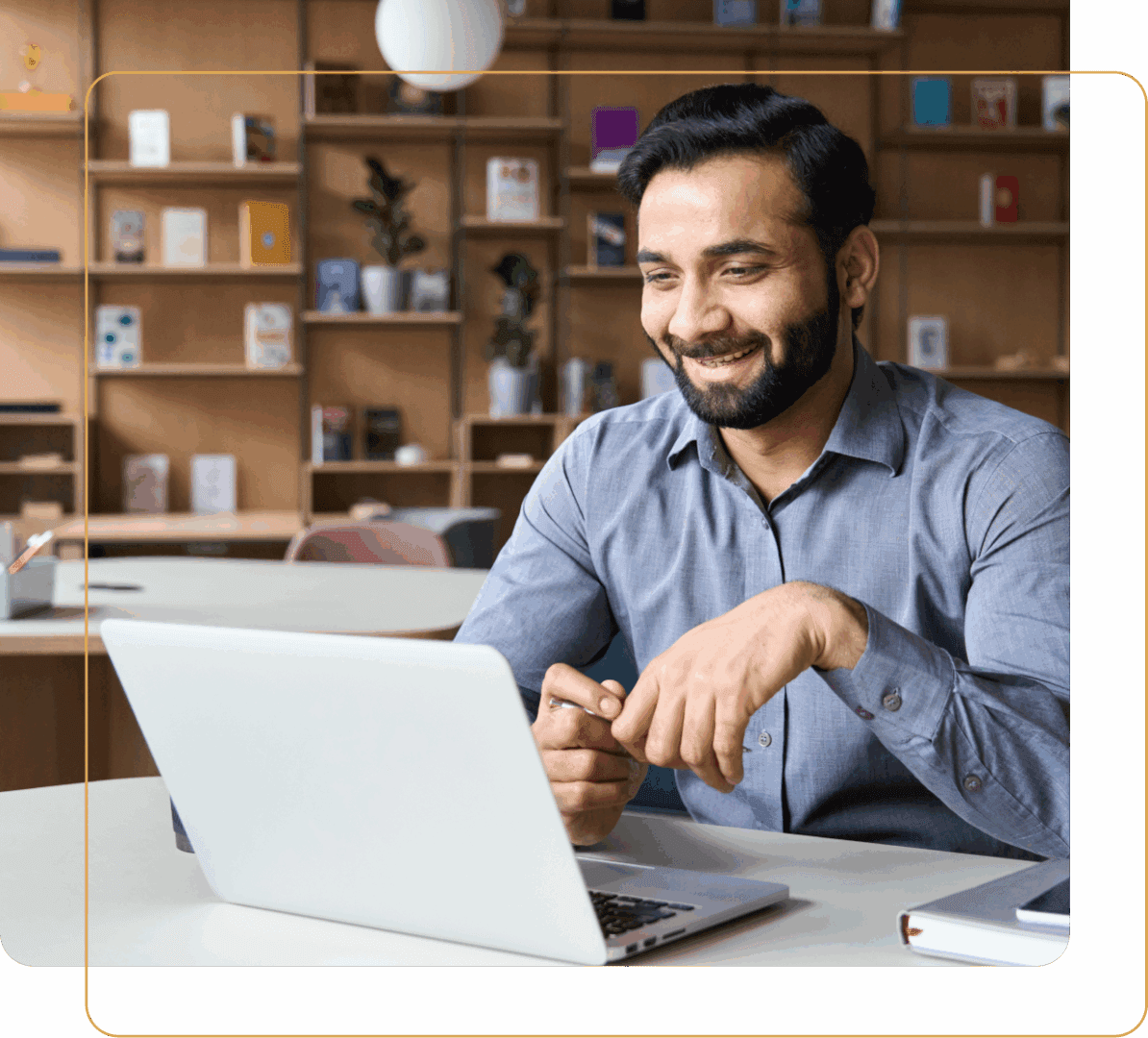 A man smiling while working on a laptop in a cozy office.