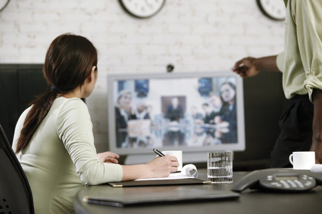A woman watching a TV screen while taking notes.