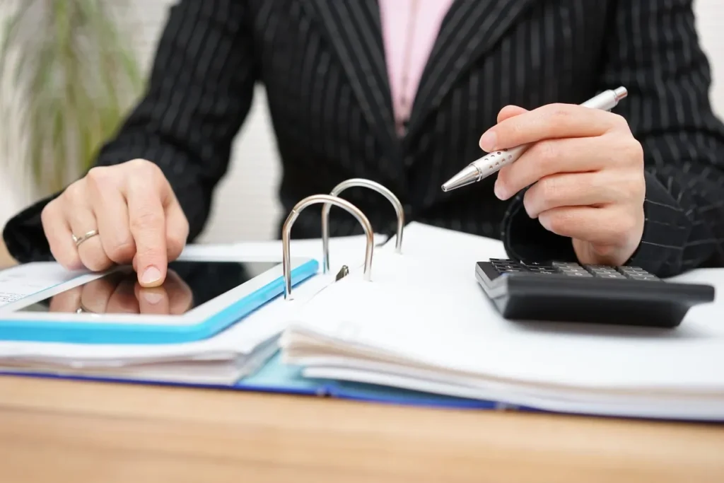 Person using a calculator and tablet with open binder on desk.