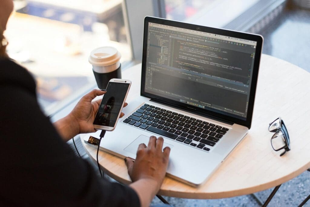 Person coding on laptop while holding phone