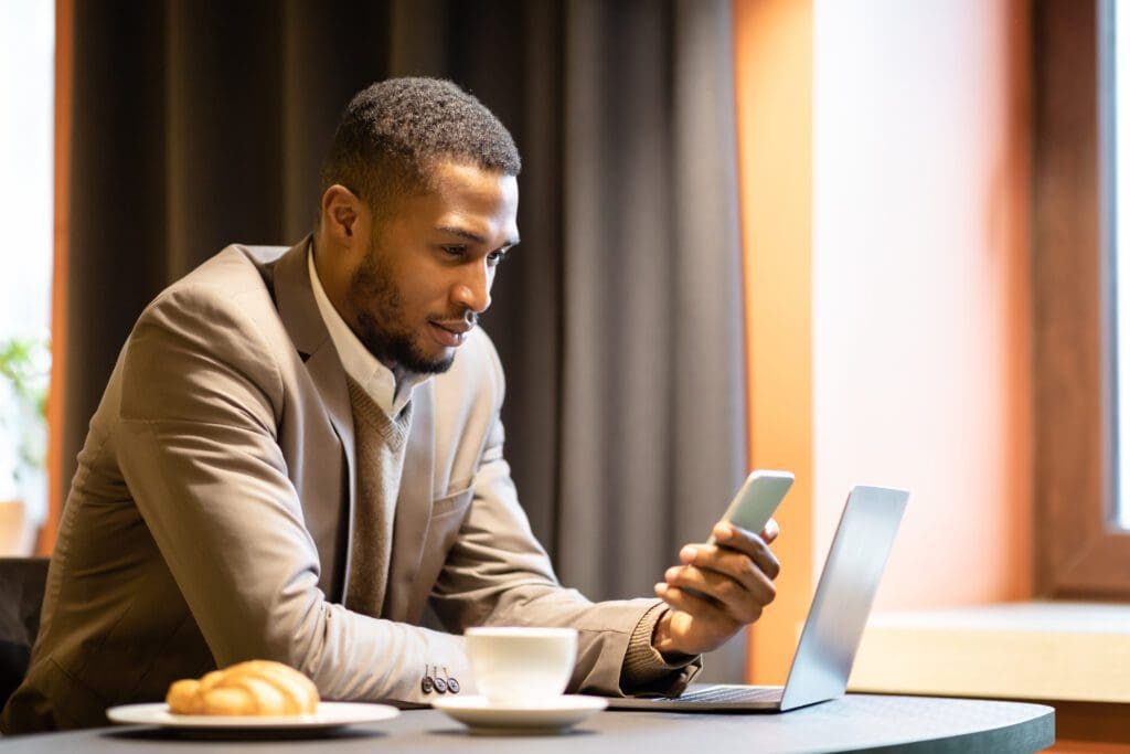Man checking phone beside laptop and coffee