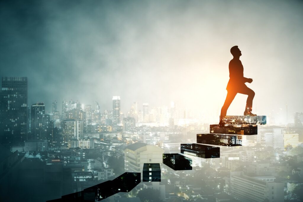 Silhouette of a person climbing rising steps made of city buildings against a glowing skyline