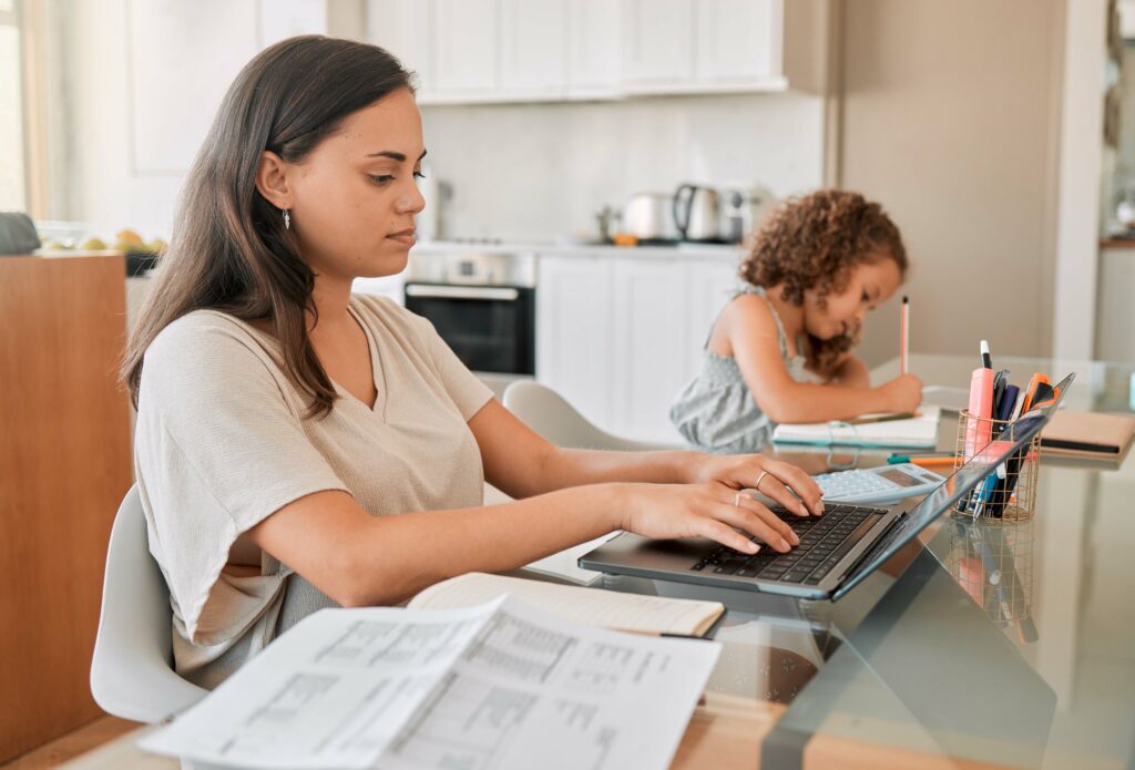 Mother managing work-life balance at the kitchen table while her child studies