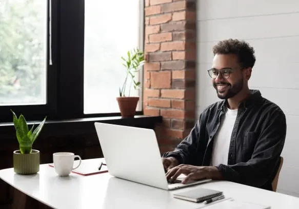 Man working on a laptop in a cozy office with brick walls.