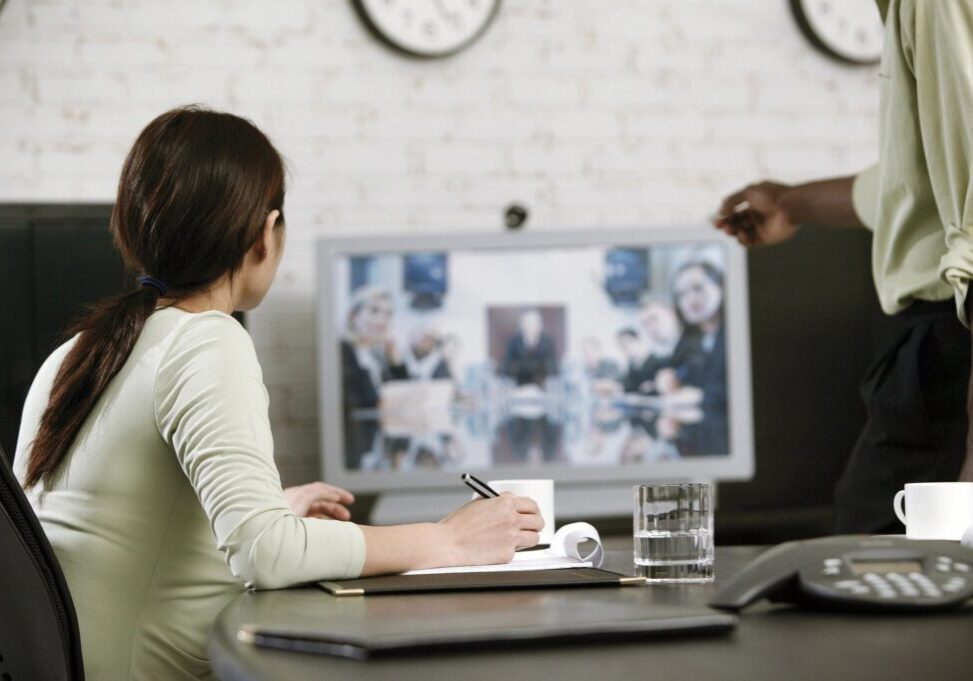 A woman watching a TV screen while taking notes.