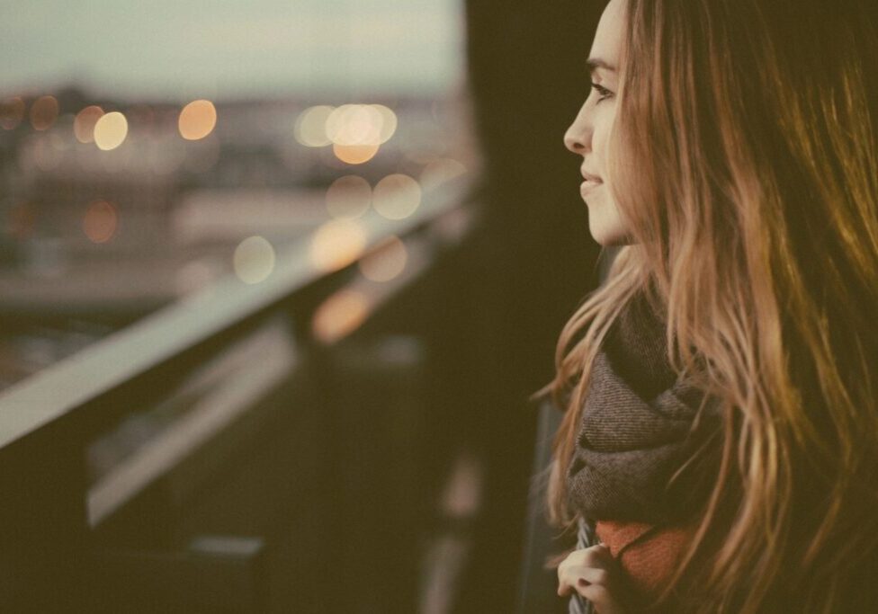 Woman gazing from balcony at sunset.