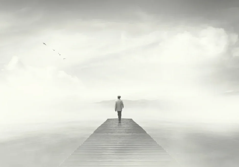 A person standing alone on a dock extending into foggy water.