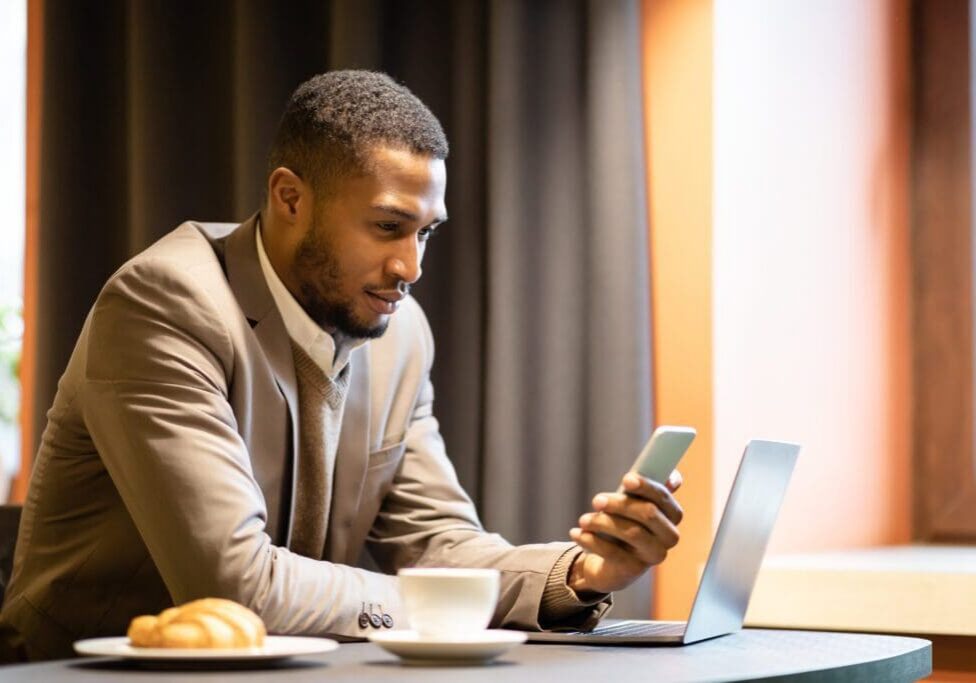 Man checking phone beside laptop and coffee