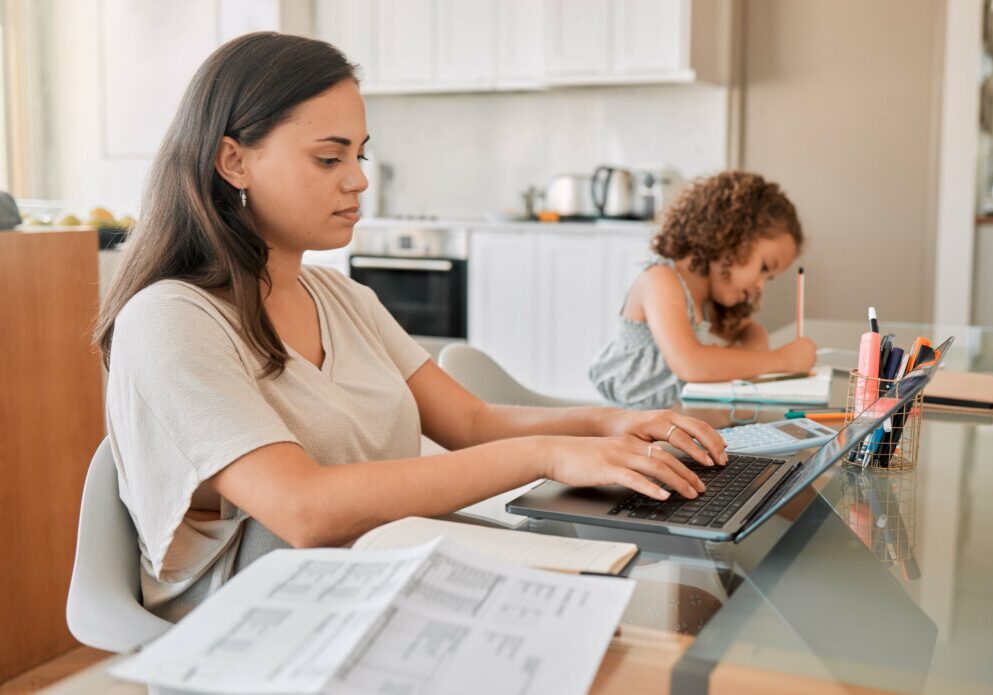Mother managing work-life balance at the kitchen table while her child studies